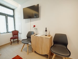 A modern room with a flat-screen TV mounted on the wall, a wooden desk with a vase of flowers, and two black chairs. - Apartment  by Interhome (Porto)