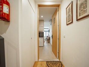 Un pasillo que conduce a una cocina con un extintor en la pared, una puerta con felpudo y un cuadro enmarcado en la pared.