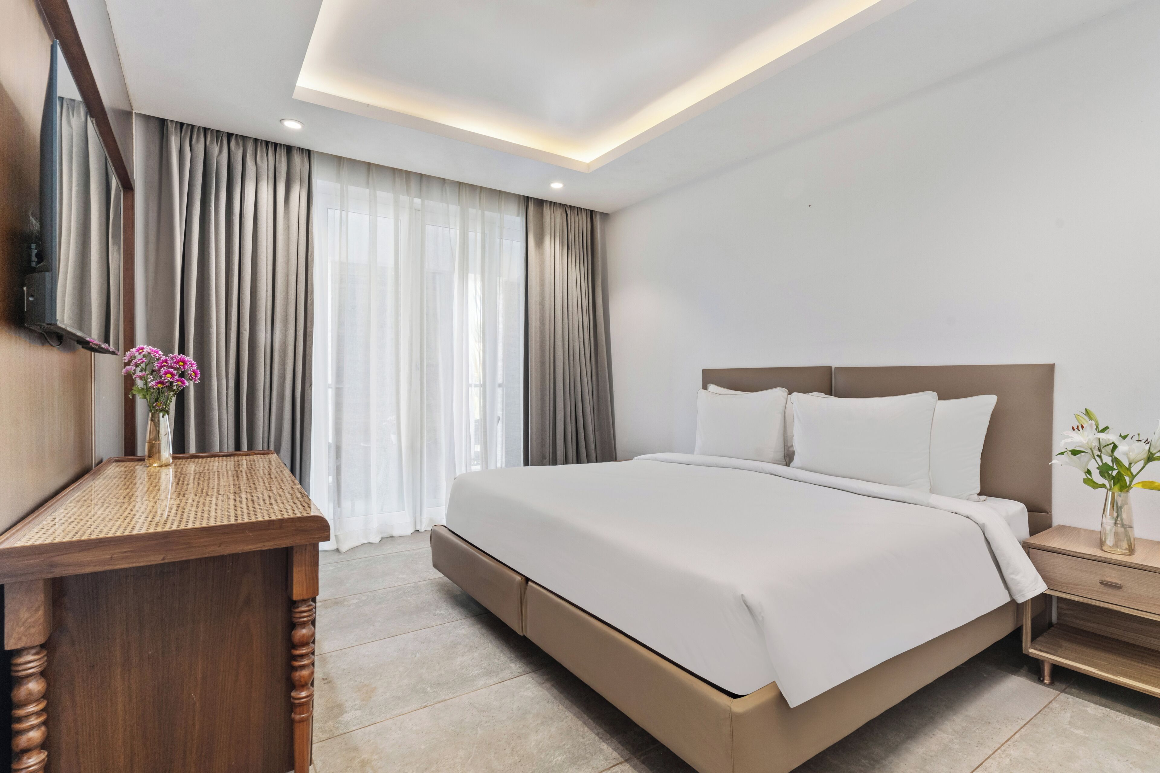 Una habitación de hotel moderna con una cama grande, una mesita de noche de madera, un televisor de pantalla plana y una ventana con cortinas.
