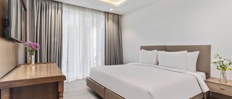 Una habitación de hotel moderna con una cama grande, una mesita de noche de madera, un televisor de pantalla plana y una ventana con cortinas.