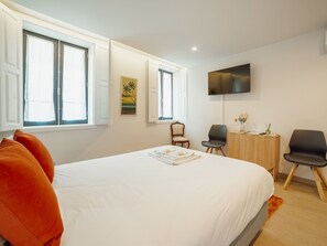 A bedroom with a large bed, two windows, a desk, a chair, and a television on the wall. - Apartment  by Interhome (Porto)