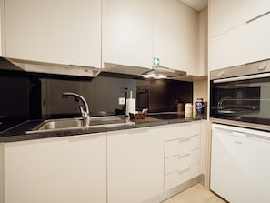 Eine moderne Küche mit Spüle aus Edelstahl, integriertem Backofen und weißen Schränken.