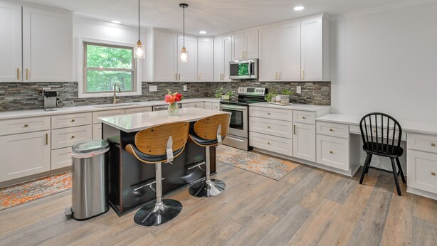 Ett modernt kök med vita skåp, en diskho i rostfritt stål, en mikrovågsugn och ett stort fönster.