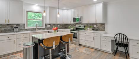 A modern kitchen with white cabinets, a stainless steel sink, a microwave, and a large window.