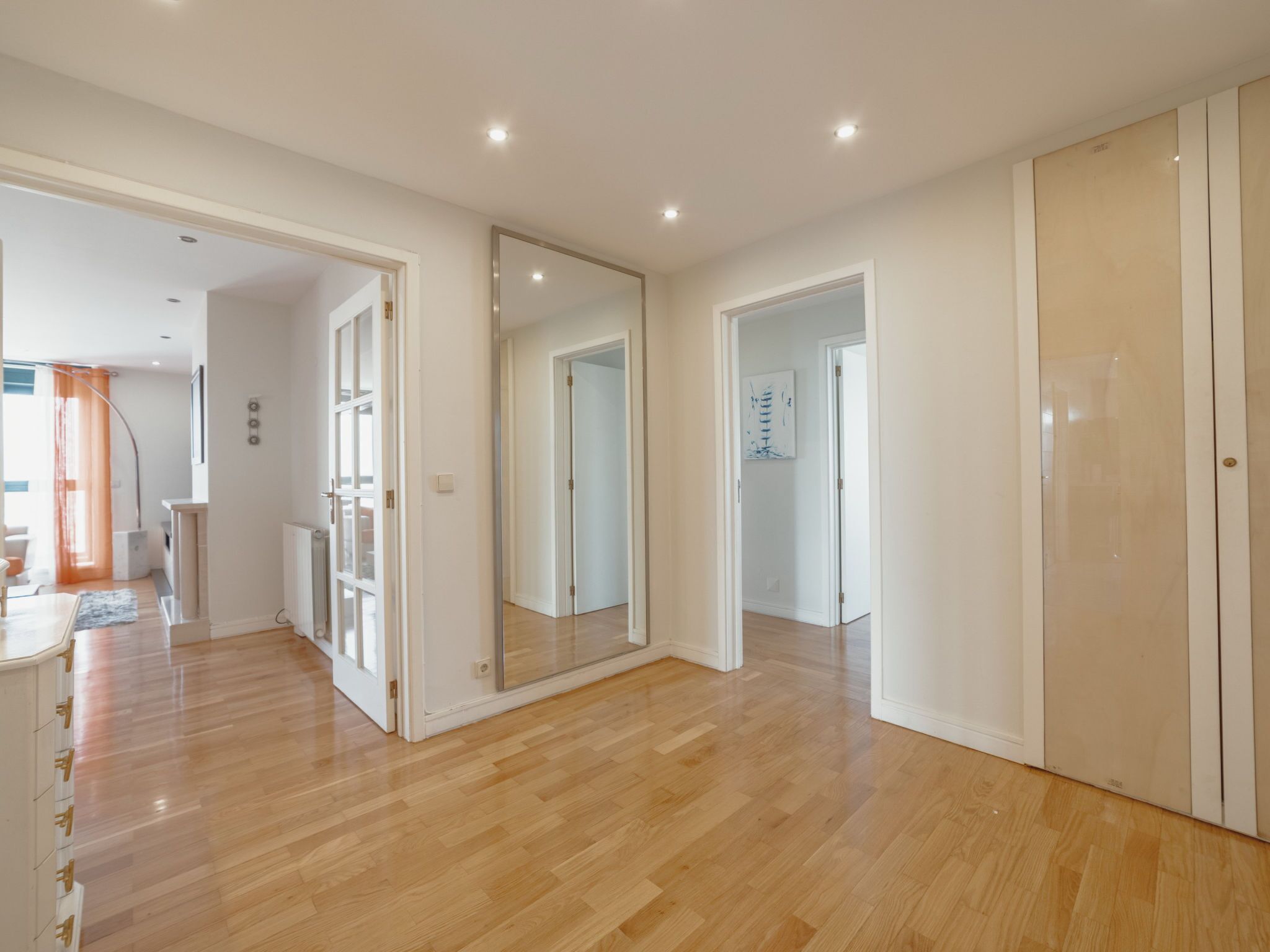 Une pièce spacieuse avec un plancher en bois, des murs blancs et un grand miroir.