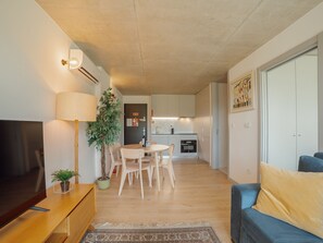 Un salon moderne doté d’un téléviseur à écran plat, d’une lampe, d’un canapé et d’un coin repas avec des chaises et une table.
