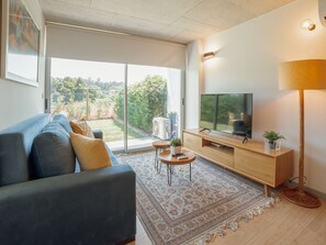 Un salon moderne avec un canapé, un téléviseur et une vue sur un jardin grâce à de grandes fenêtres.