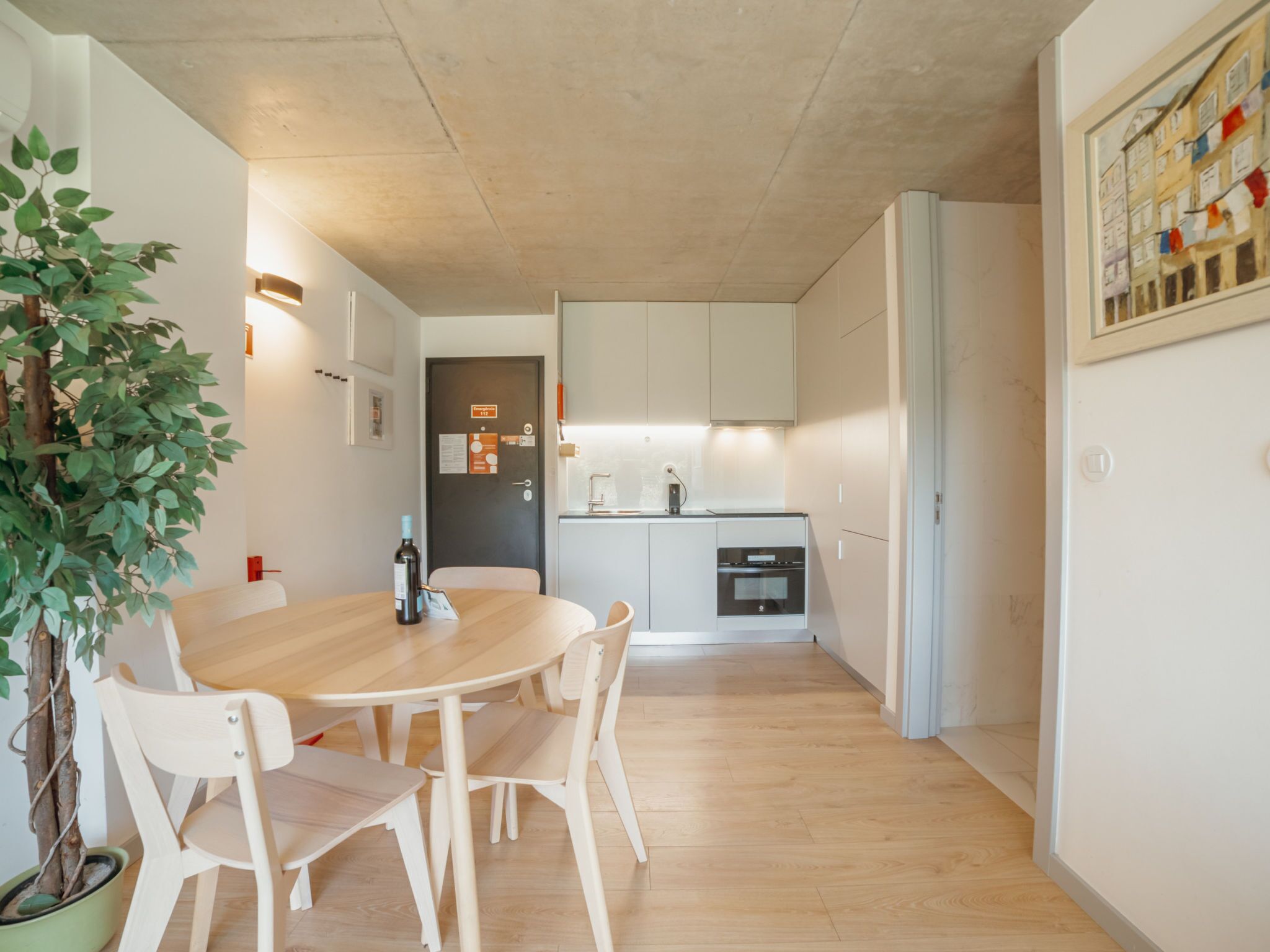 A modern kitchen with white cabinets, a dining table with chairs, and a potted plant.