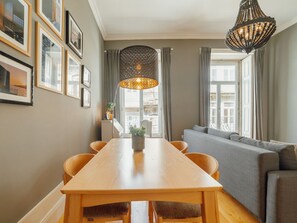 A dining area with a wooden table and chairs, a hanging pendant light, and a sofa with a view of the street. - Apartment  by Interhome (Porto)