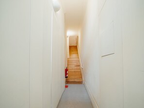 Ein schmaler Flur mit weißen Wänden, einer Holztreppe und einem roten Feuerlöscher am Boden.