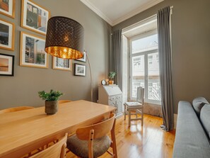 A cozy living room with a wooden dining table, a sofa, and a large window with curtains. - Apartment  by Interhome (Porto)