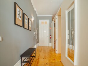 A hallway with wooden flooring, a bench, framed artwork on the wall, and a white door at the end. - Apartment  by Interhome (Porto)