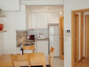 Una cocina compacta con armarios blancos, microondas, refrigerador y un pequeño comedor con mesa y sillas.