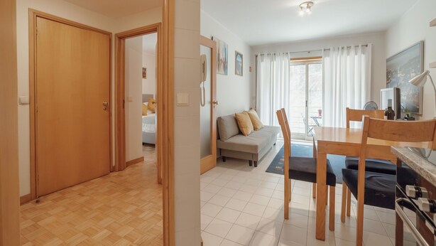 Ein geräumiger Wohnbereich mit Sofa, Esstisch und Stühlen, eine Küchenzeile mit Herd sowie ein Flur, der in einen weiteren Raum führt.