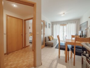 Ein geräumiger Wohnbereich mit Sofa, Esstisch und Stühlen, eine Küchenzeile mit Herd sowie ein Flur, der in einen weiteren Raum führt.
