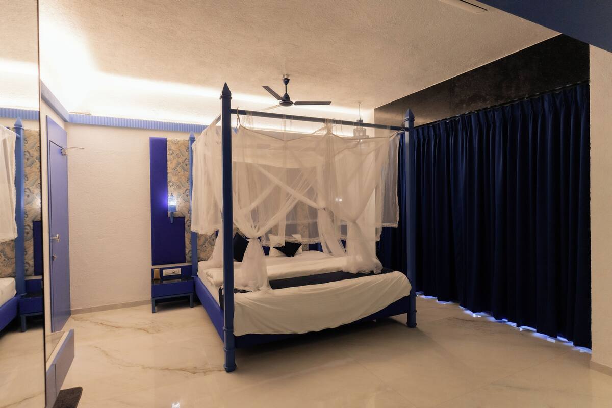 A four-poster bed with a canopy, a ceiling fan, and a dark curtain on a window.