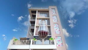 Un edificio de varios pisos con balcones, una estructura de vidrio distintiva en la planta baja y un cielo azul despejado.