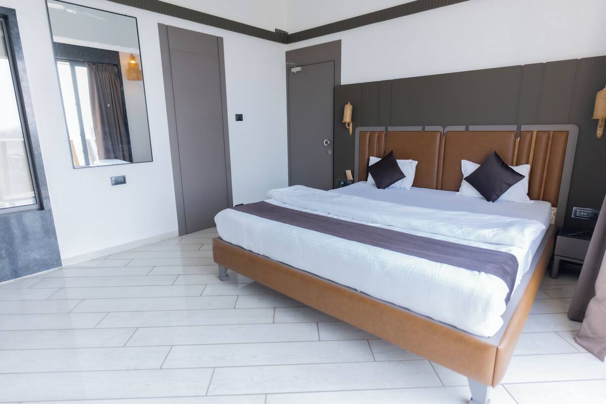 A modern hotel room with a large bed, a mirror, a wardrobe, and a bedside table.