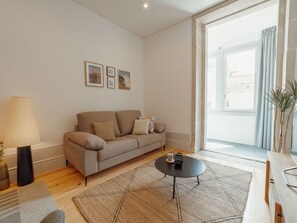 A modern living room with a sofa, a coffee table, and a lamp. There are framed pictures on the wall and a large window with curtains. - Apartment  by Interhome (Porto)