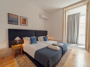 Ein Hotelzimmer mit einem großen Bett, zwei Nachttischen, einer Lampe, einem Fenster mit Vorhängen und Kunstwerken an der Wand.