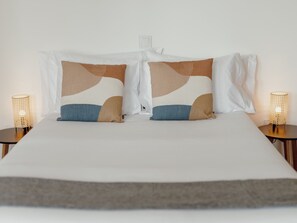 Ein Bett mit einer weißen Matratze, zwei Kissen mit abstrakten Mustern und zwei Nachttische mit gewebtem Dekor.