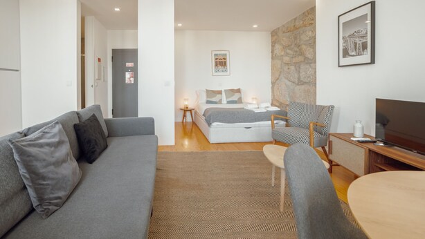 Et moderne hotelværelse med en grå sofa, en seng, et lille bord og et fjernsyn.