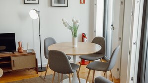 En moderne stue med et rundt spisebord, grå stole, et fladskærms-tv, en gulvlampe og en vase med blomster.