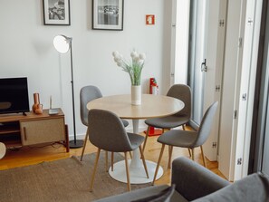 Ein modernes Wohnzimmer mit einem runden Esstisch, grauen Stühlen, einem Flachbildfernseher, einer Stehlampe und einer Blumenvase.