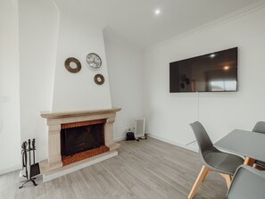 Ein modernes Wohnzimmer mit Kamin, einem an der Wand montierten Flachbildfernseher und einem Essbereich mit Tisch und Stühlen.