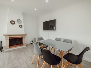 A modern living room with a fireplace, a flat-screen TV mounted on the wall, and a dining table with chairs. - Apartment  by Interhome (Porto)