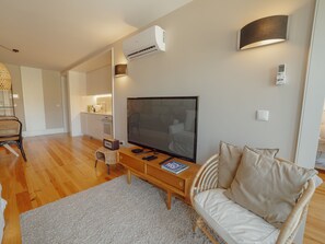 A modern living room with a flat-screen TV, a sofa, a coffee table, and a dining area with a kitchen in the background. - Apartment  by Interhome (Porto)