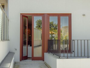 A building entrance with a sliding glass door, a small outdoor balcony with a metal railing, and a concrete ledge. - Apartment  by Interhome (Porto)