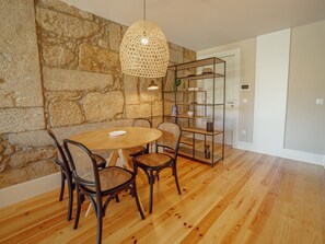 A dining area with a stone wall, a round wooden table, four wicker chairs, a hanging light fixture, and a glass-fronted shelving unit. - Apartment  by Interhome (Porto)