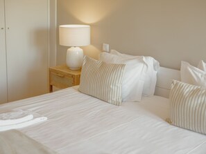 A neatly made bed with white linens and striped pillows, a bedside lamp, and a wooden nightstand. - Apartment  by Interhome (Porto)