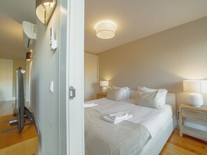 A hotel room with a large bed, bedside lamps, a flat-screen TV, and a wooden floor. - Apartment  by Interhome (Porto)