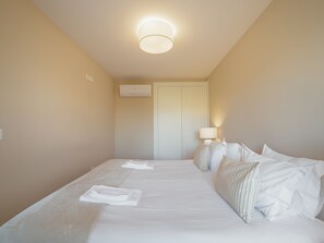 A hotel room with a bed, pillows, a bedside lamp, and an air conditioning unit. - Apartment  by Interhome (Porto)