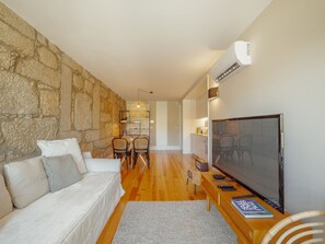 A modern living room with a stone wall, a white sofa, a dining area with chairs, a TV, and a wooden coffee table. - Apartment  by Interhome (Porto)