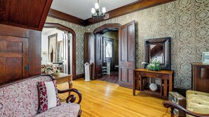 A room with a wooden floor, a patterned sofa, a wooden console table, and a mirror. - Historic Victorian Cottage, 1 Mi to Niagara Falls (Niagara Falls)