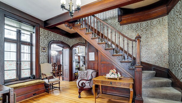 A grand staircase with ornate woodwork, a bench, and a table with flowers. - Historic Victorian Cottage, 1 Mi to Niagara Falls (Niagara Falls)