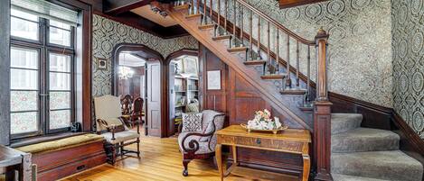 Una imponente escalera con intrincados adornos de madera, un banco y una mesa con flores.