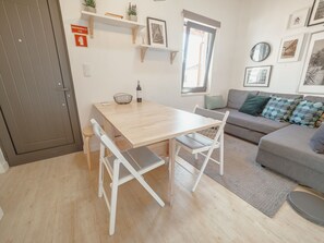 Un salon moderne avec une table à manger en bois, des chaises blanches, un canapé gris agrémenté de coussins à motifs et une petite fenêtre.