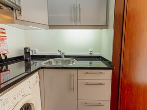 Eine kompakte Küche mit Einbauwaschmaschine, Spüle aus Edelstahl und Holzschrank.