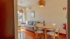 A modern living room with a wooden floor, a grey sofa, a round wooden table with chairs, and two hanging wicker lamps. - Apartment  by Interhome (Porto)