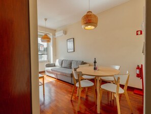 Ein modernes Wohnzimmer mit Holzboden, einem grauen Sofa, einem runden Holztisch mit Stühlen und zwei hängenden Korbstühlen.