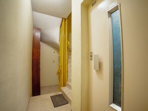 Ein schmaler Flur mit einer Holztür, einem gelben Vorhang und einem Fenster mit rauer Glasverglasung.