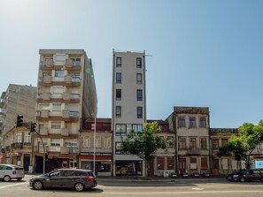 Ein mehrgeschossiges Gebäude mit Balkonen, Blick auf die Straße und ein Auto im Vordergrund.