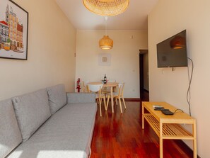 A living room with a sofa, a dining table with chairs, a TV mounted on the wall, and a hanging light fixture. - Apartment  by Interhome (Porto)