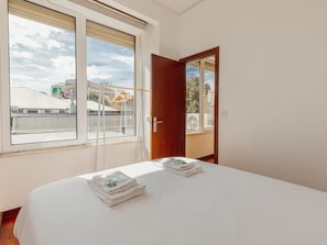 A hotel room with a large bed, a window with a view of buildings, and a door. - Apartment  by Interhome (Porto)