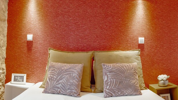 Ein Bett mit zwei Kissen, ein Nachttisch mit einem gerahmten Gegenstand und ein kleiner Tisch mit einer Vase.