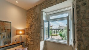 Ein Zimmer mit Steinwand, einem Fenster mit freiem Blick, einer Couch mit Kissen und einer Lampe auf einem Beistelltisch.